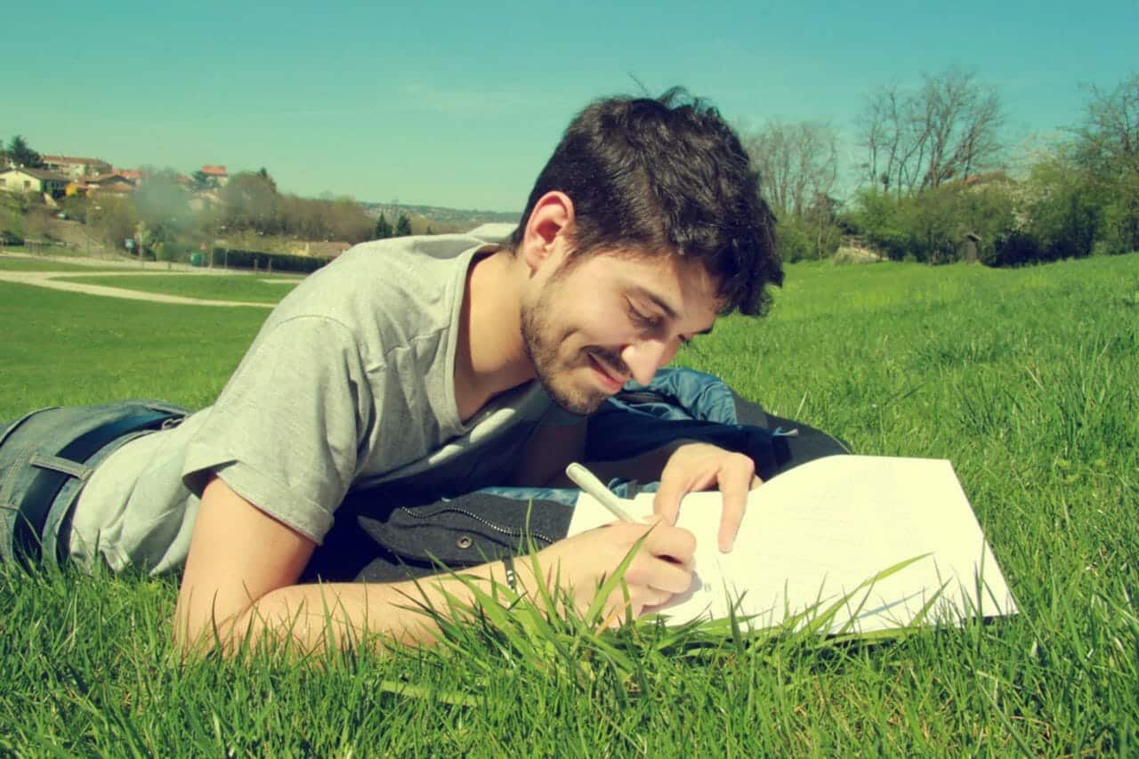 young man sitting in grass writing