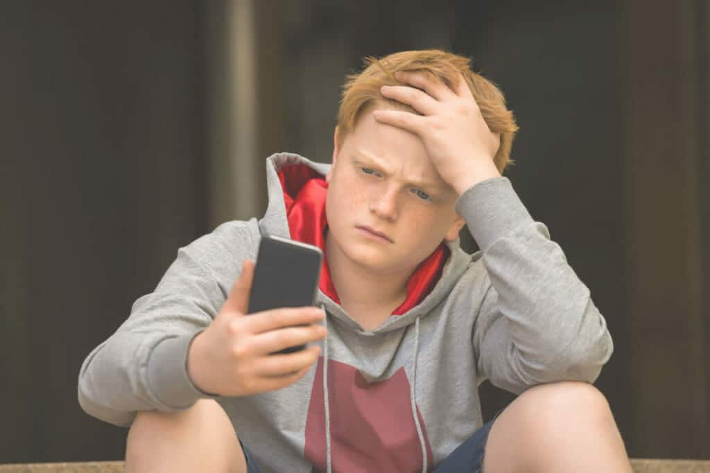 Upset young teenage boy looking at his phone