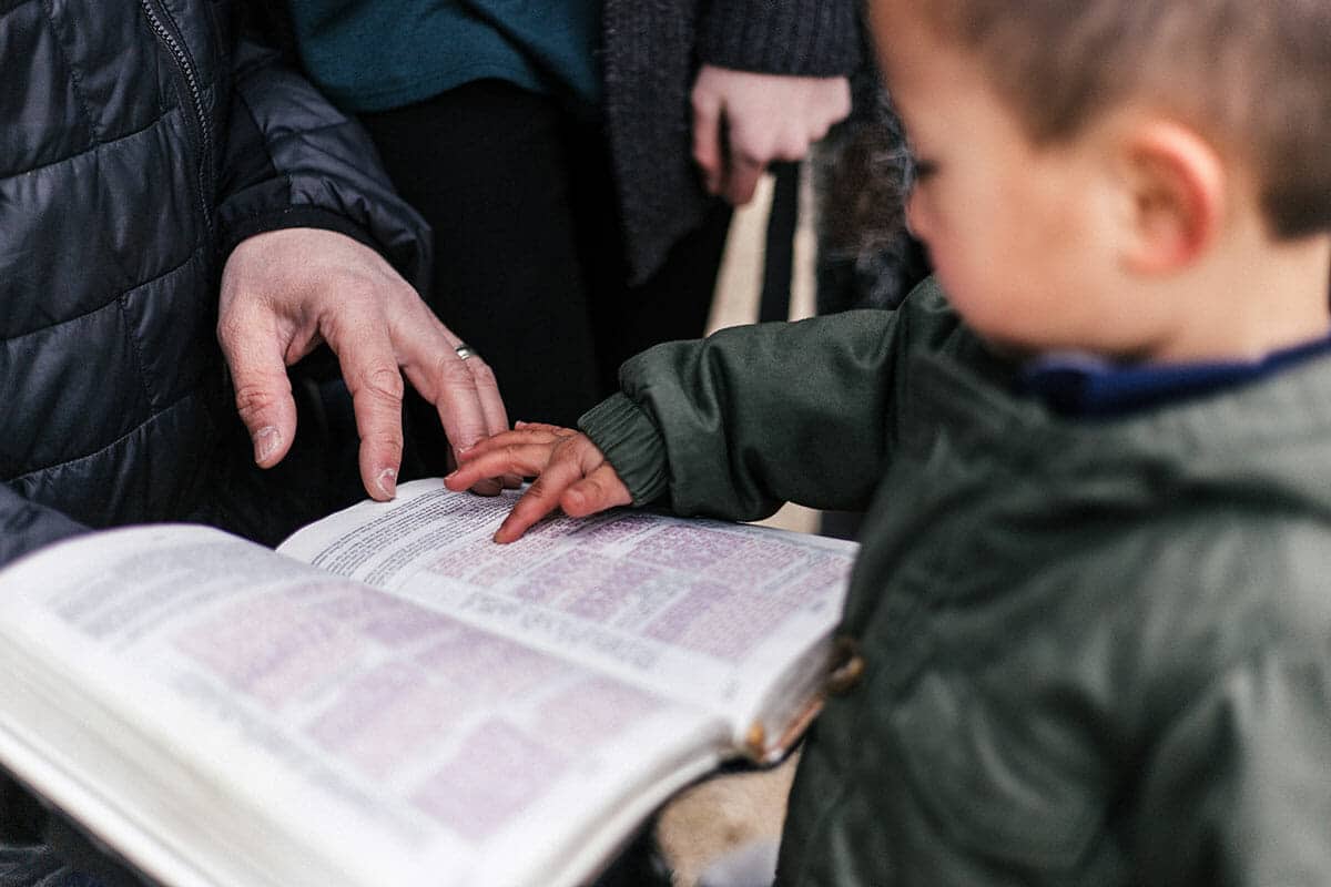 Parent and Child holding hands on the Bible