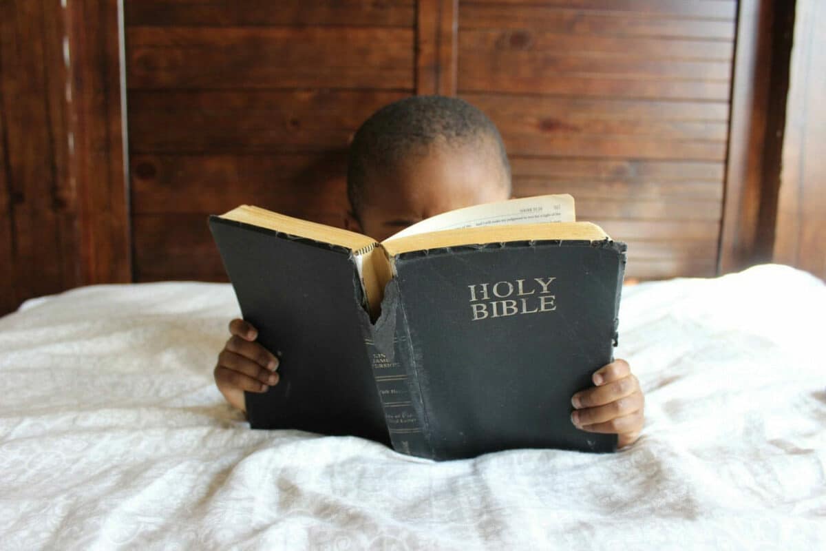 Little boy reading a Bible in bed